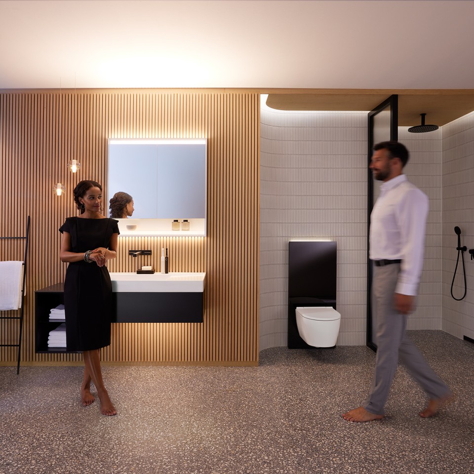 Mann og kvinne i perfekt opplyst bad med Geberit ONE baderomsmøbler, servant og toalett (© Geberit)