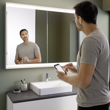 Mannen styrer belysningen av Geberit ONE speilskapet med sin smarttelefon (© Geberit)